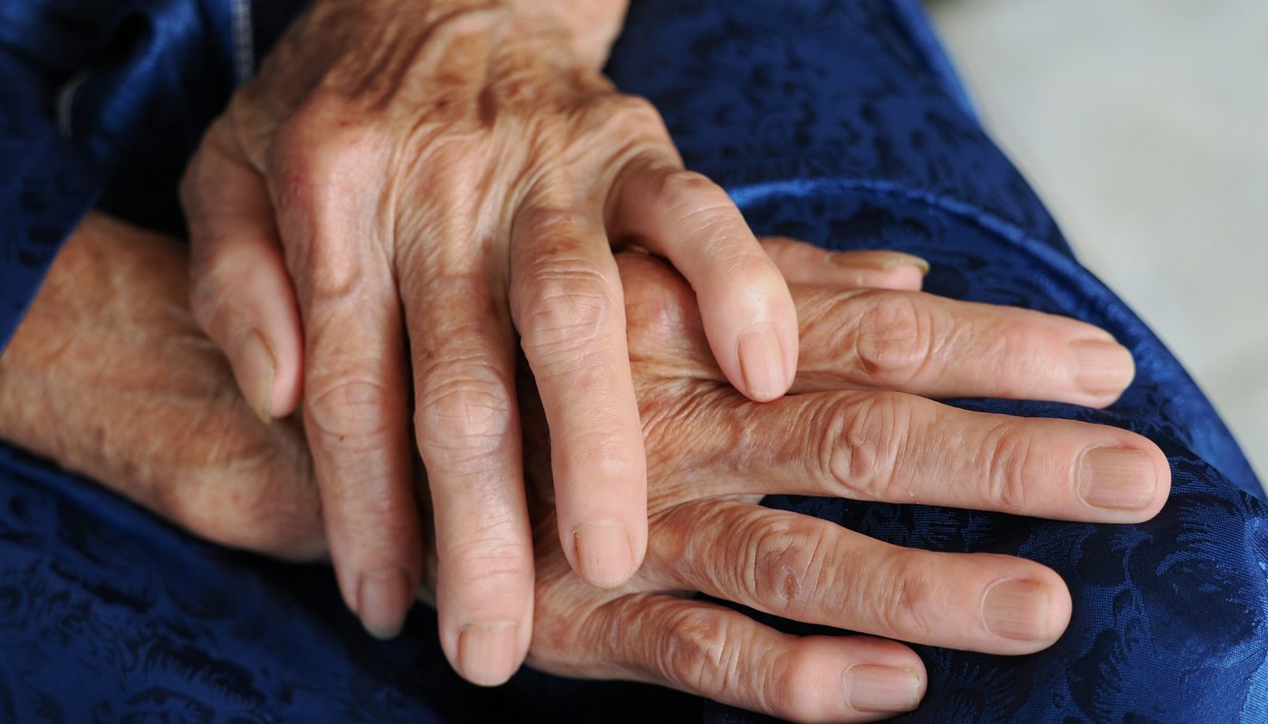 Mains d'une personne âgée posées sur un tissu bleu